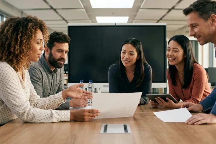 Five colleagues gathered around a table, discussing a document together